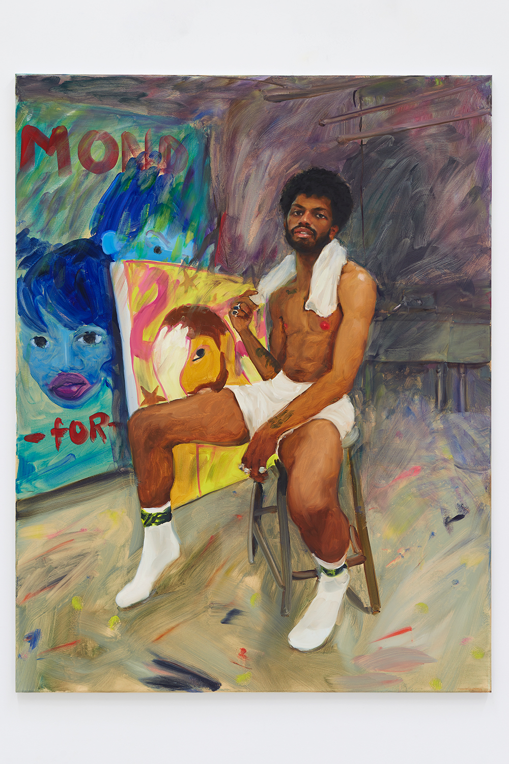 An oil painting of a Black figure in white tube socks and white athletic or boxer shorts. They are perched, legs open, on a stool, and looking at the viewer with lips open slightly. They have a short afro and beard, and are wearing multiple rings on their fingers; one hand holds a short towel around their neck. We can see tattoos or paint stains on their two forearms. The floor is paint-stained, and in the background are two large-scale paintings, in bright colors, with Black figures, obscured text, and a flamingo painted on them.