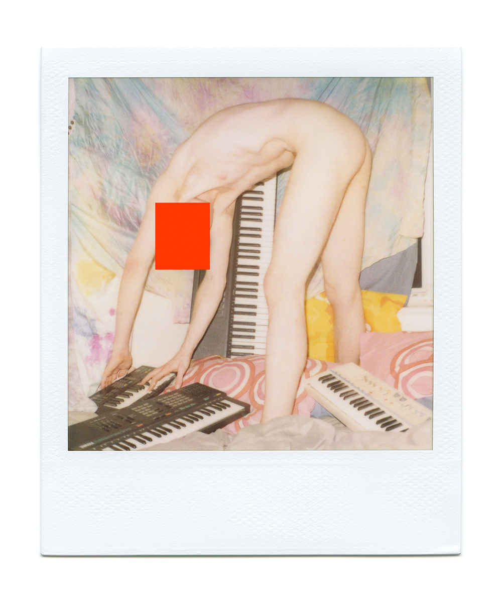 A slightly washed out polaroid of a young white twink, face obscured with a bright red box digitally added, completely naked and bending over to play a small electric Yamaha keyboard on the floor; the twink’s legs obscure any genitals. There are several more larger keyboards also on the floor, which is covered in pillows. In the background, a tye-dye blanket covers the majority of the frame, with one more larger keyboard propped up against it. 