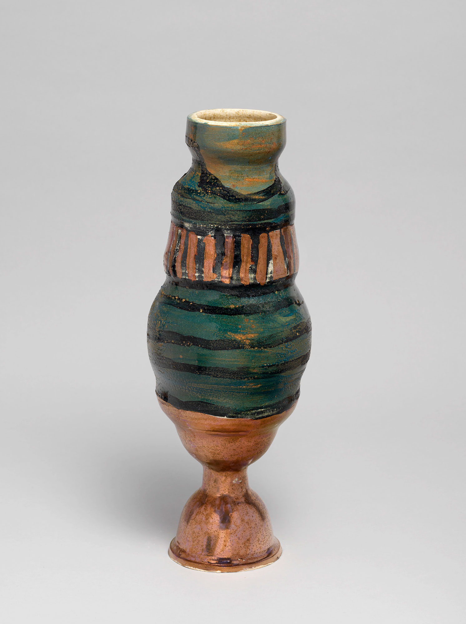 A vase with a base painted bronze, while the body is dark green and orange with black lines.