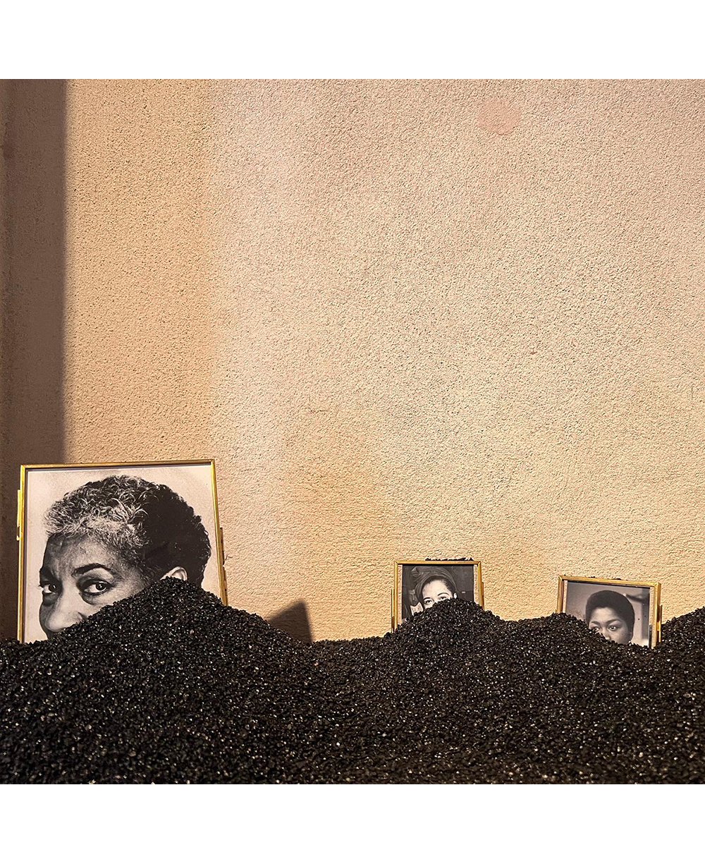 Black sand partially covers three framed photos of women