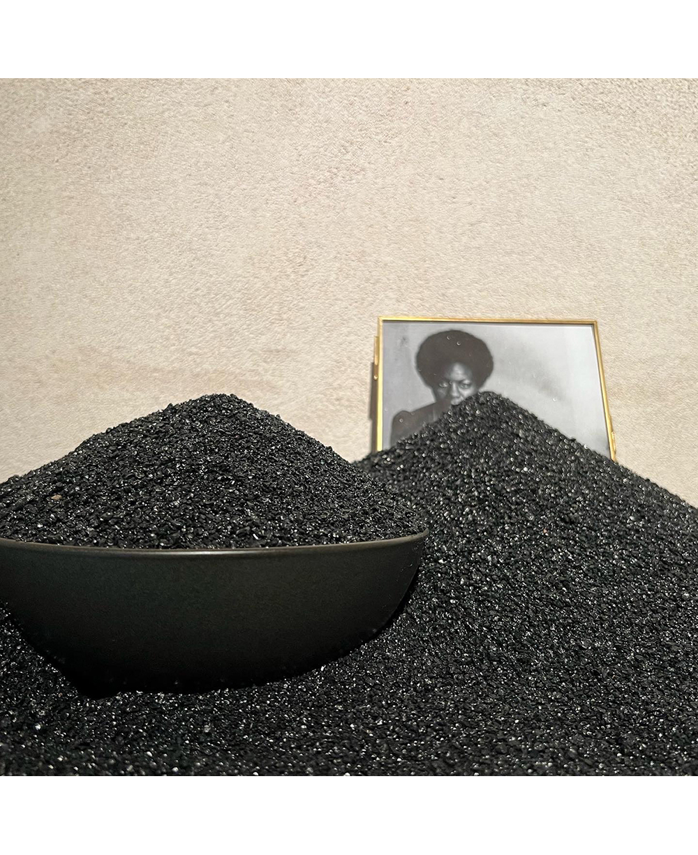 A bowl overflowing with black sand partially covers a framed photo of a dark skinned woman 