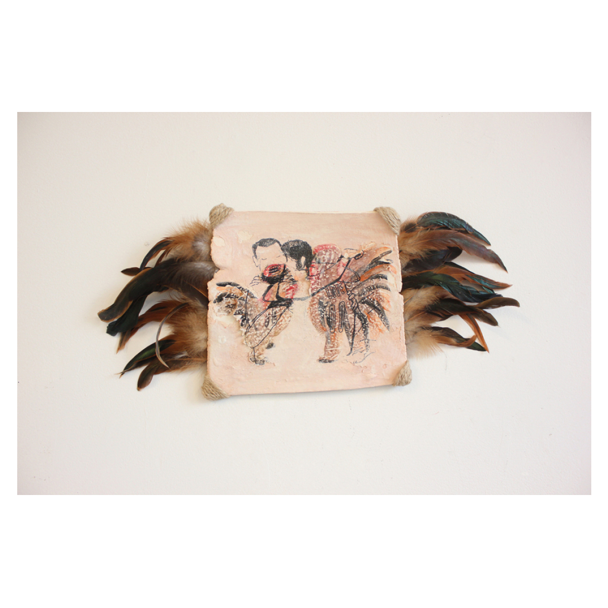 Wide rectangular tan ceramic plate? with hemp cord wrapped around the corners and feathers poking out from the behind on the left and right sides. The ceramic has a red brown and black decal with a drawing of two chickens with human heads embracing each other.