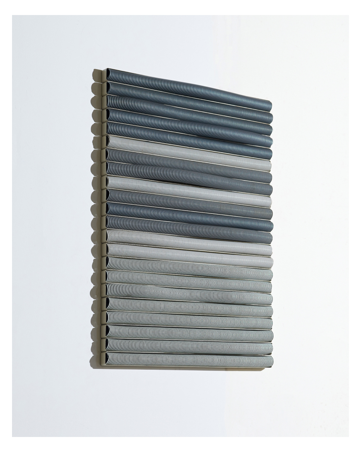 Mounted on a wall  are multiple rows of parallel horizontal gray vacuum hoses held together with office cubicle caps.