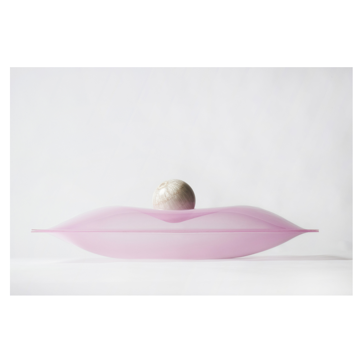 Two light pink semi transparent skylight domes are back to back creating a pillow shape that holds a pearlescent and cream colored bowling ball..