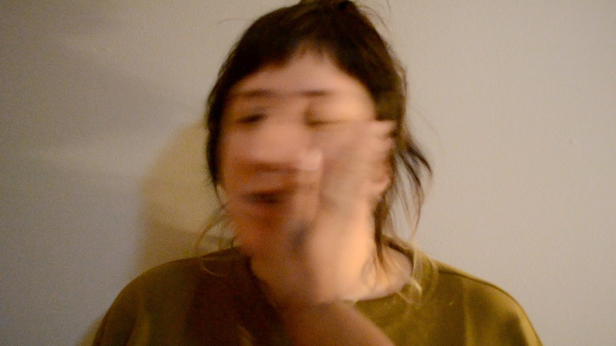 A photo blurred by movement of a Black hand slapping the face of a white woman with brown hair and short bangs and yellow/green shirt from the point of view of the Black person.